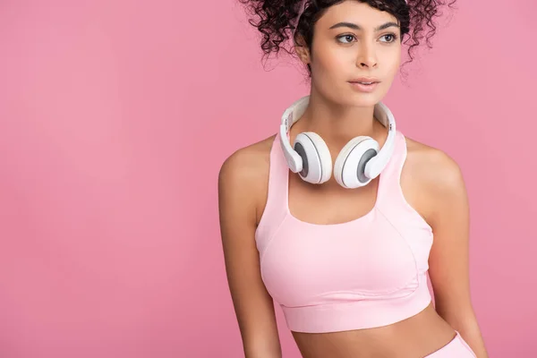 Curly young woman in wireless headphones looking away isolated on pink — Stock Photo