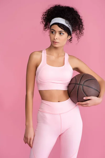 Encaracolado jovem segurando basquete isolado em rosa — Fotografia de Stock