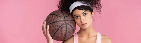 Rizado mujer joven sosteniendo baloncesto aislado en rosa, bandera horizontal - foto de stock