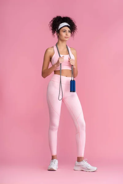 Full length of curly young sportswoman standing with jumping rope on pink — Stock Photo