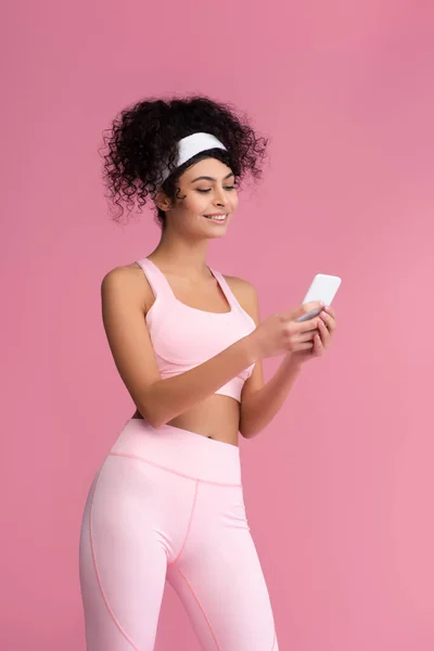 Fröhliche junge Sportlerin mit Smartphone isoliert auf rosa — Stockfoto