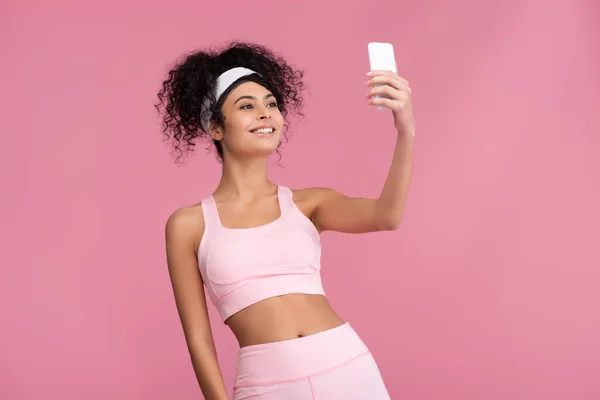 Счастливая молодая спортсменка делает селфи на смартфоне изолированы на розовый — стоковое фото