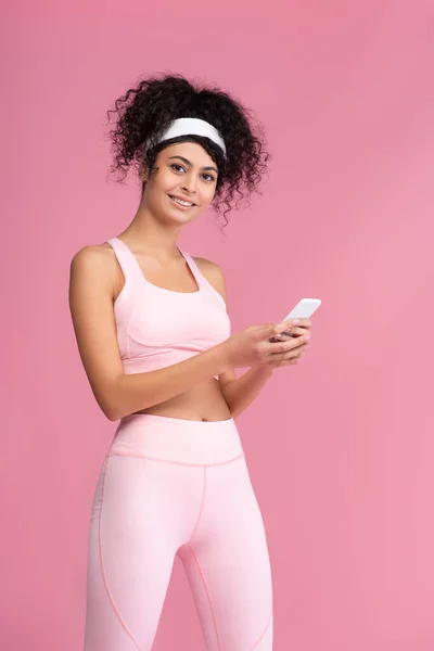 Happy young sportswoman using smartphone isolated on pink — Stock Photo