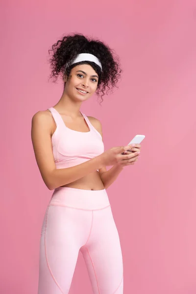 Happy young sportswoman using smartphone isolated on pink — Stock Photo