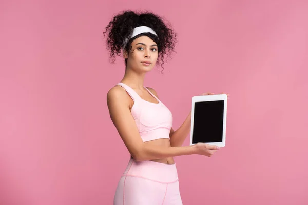 Young sportswoman holding digital tablet with blank screen isolated on pink — Stock Photo