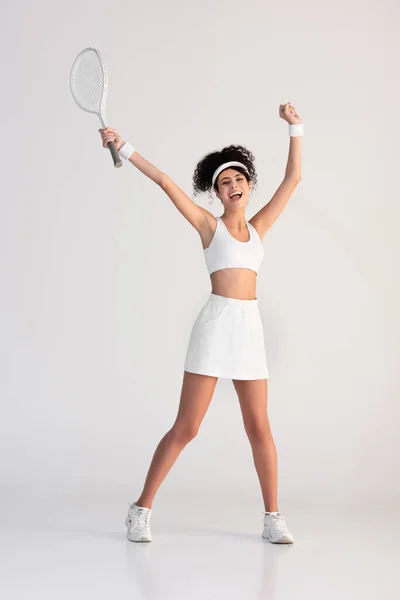 Full length of excited player in sportswear holding tennis racket and jumping on white — Stock Photo