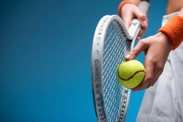 Partial view of sportive young woman holding tennis racket and ball while playing on blue — Stock Photo