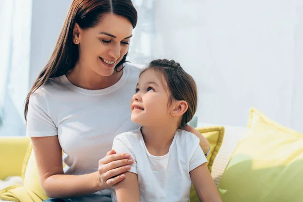 Madre feliz mirando a la hija alegre en casa - foto de stock