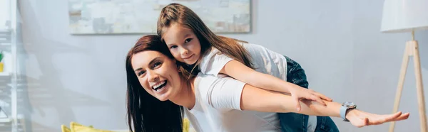 Feliz madre e hija con las manos extendidas mirando a la cámara mientras se arrastra junto con la imagen borrosa en el fondo, pancarta - foto de stock