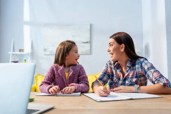 Emocionados madre e hija con la boca abierta mirándose en el escritorio con la computadora portátil borrosa en primer plano — Stock Photo