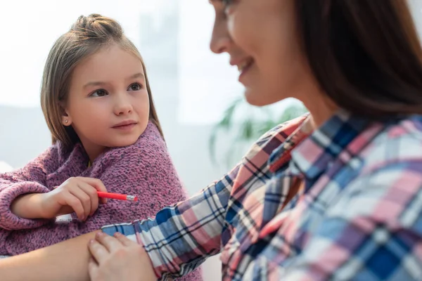 Tochter mit Bleistift blickt verschwommene Mutter im Vordergrund an — Stockfoto