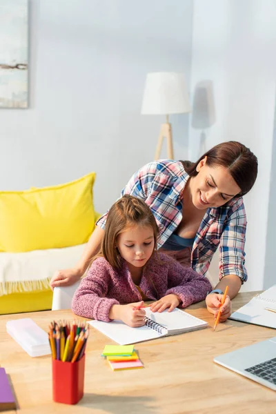 Sorrindo mãe e filha olhando para notebook na mesa perto de laptop em primeiro plano turvo — Fotografia de Stock