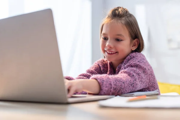 Sorrindo menina digitando no laptop na mesa em primeiro plano desfocado — Fotografia de Stock