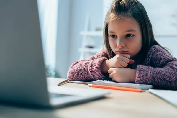 Chica molesta mirando a la computadora portátil en el escritorio en primer plano borrosa - foto de stock