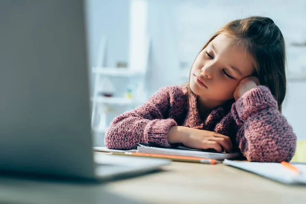 Menina cansada na mesa com laptop desfocado em primeiro plano — Fotografia de Stock