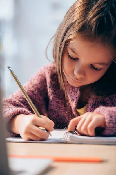 Дівчина з олівцем, що пише в блокноті за столом на розмитому передньому плані — стокове фото