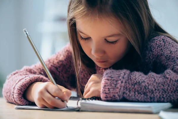 Menina com lápis escrevendo em notebook sobre fundo embaçado — Fotografia de Stock