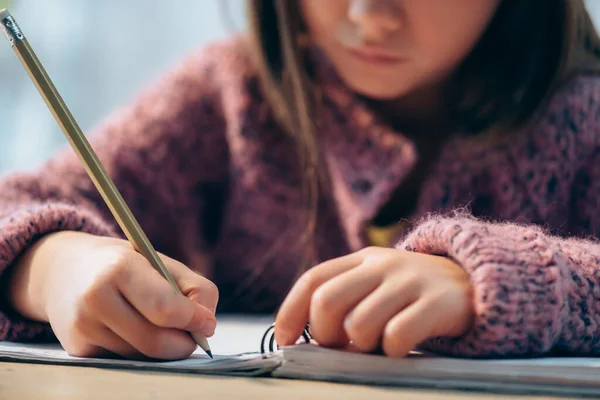 Vista cortada de menina com lápis escrevendo em notebook sobre fundo borrado — Fotografia de Stock