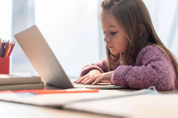 Mädchen tippt auf Laptop am Schreibtisch auf verschwommenem Vordergrund — Stockfoto