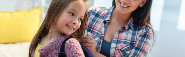 Sorrindo filha olhando para longe, enquanto a mãe colocando mochila no fundo borrado, banner — Fotografia de Stock