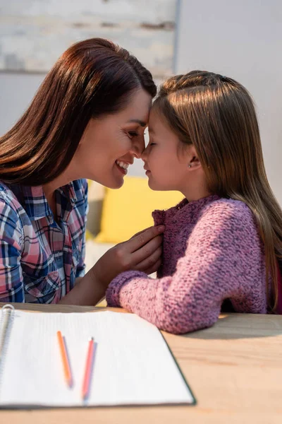 Feliz madre vistiendo a su hija cerca del escritorio con un libro borroso en primer plano - foto de stock