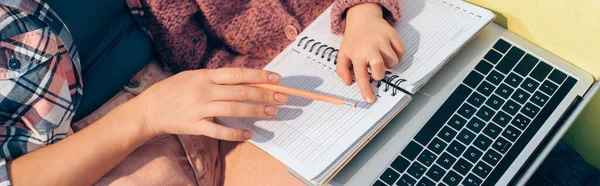 Vista ritagliata della figlia che punta con il dito al notebook vicino alla madre e al computer portatile, banner — Foto stock