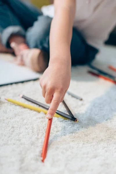 Cropped view of girl holding red colored pencil on carpet on blurred background — Stock Photo