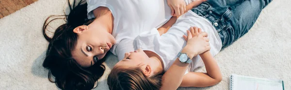 Vista aérea de la madre con los labios pucheros mirando a la hija mientras está acostada en el suelo, pancarta - foto de stock