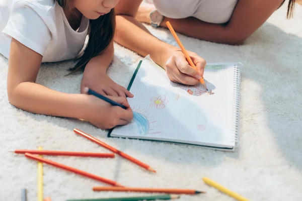 Vista ritagliata di madre e figlia con matite colorate disegno in copia libro su primo piano sfocato — Foto stock