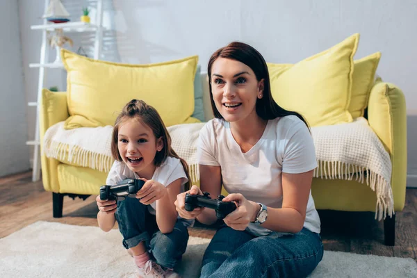 KYIV, UKRAINE - OCTOBER 19, 2020: Happy mother and daughter playing with joysticks on floor on blurred background — Stock Photo