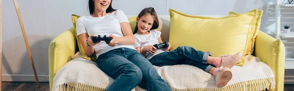 KYIV, UKRAINE - OCTOBER 19, 2020: Happy daughter with joystick looking at camera near mother on couch, banner — Stock Photo