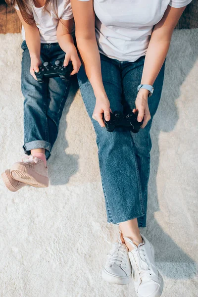 QUIIV, UCRÂNIA - OUTUBRO 19, 2020: Vista cortada de mãe e filha brincando com joysticks enquanto sentadas no chão — Fotografia de Stock