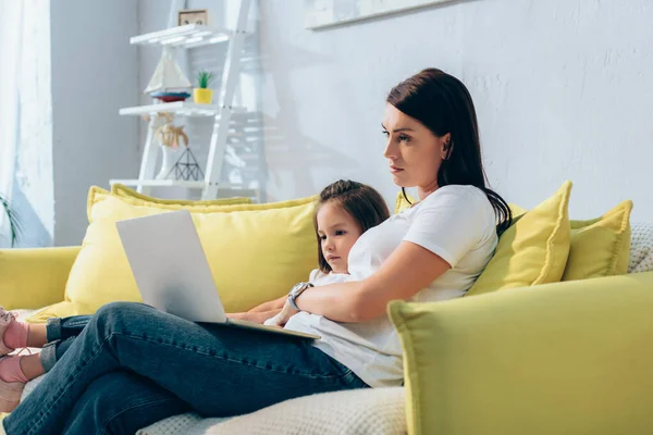 Mother and daughter looking at laptop while sitting on couch on blurred background — Stock Photo