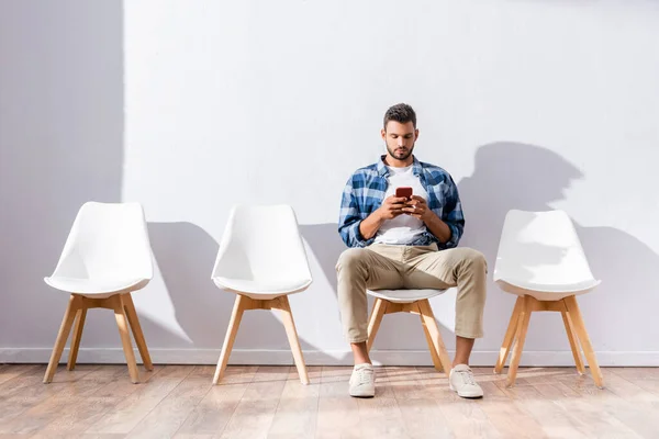 Человек в повседневной одежде с помощью смартфона во время ожидания на стуле в холле — стоковое фото