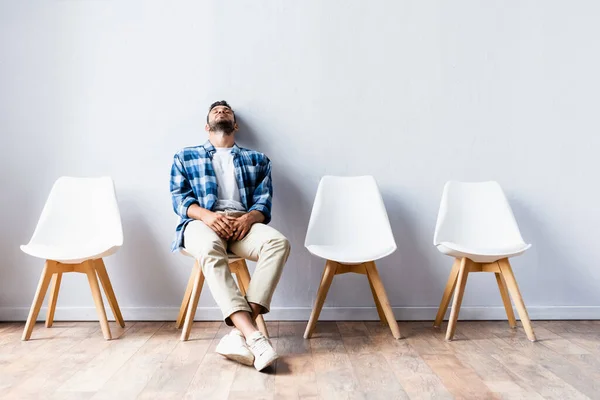 Hombre cansado sentado en la silla mientras espera en el pasillo - foto de stock