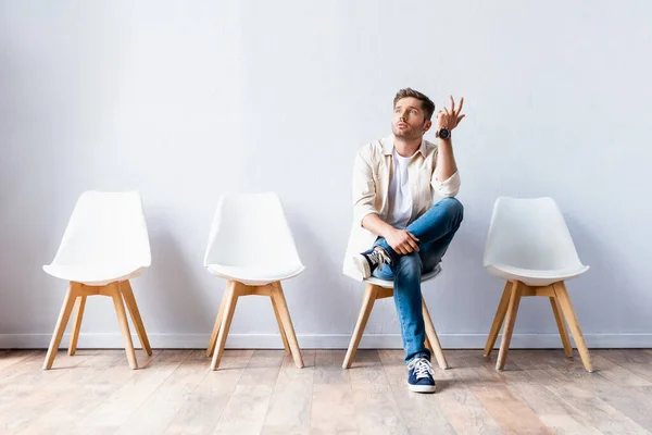 Junger Mann schaut weg, während er in Flur auf Stuhl sitzt — Stockfoto