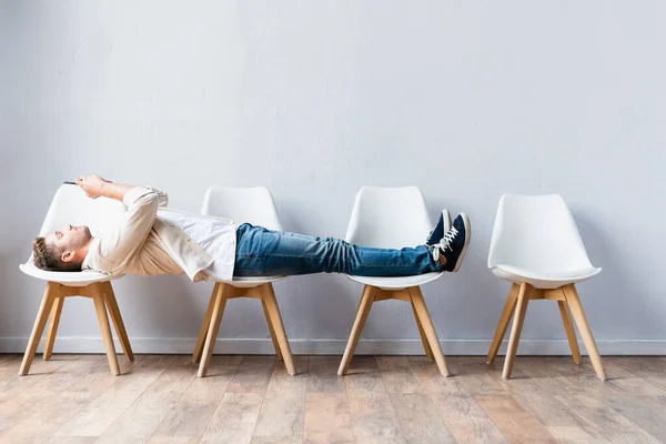 Man in casual clothes using mobile phone while lying on chairs in hall — Stock Photo