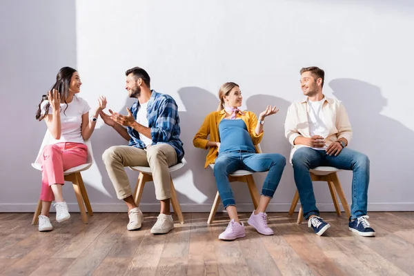 Lächelnde multiethnische Menschen unterhalten sich auf Stühlen im Saal — Stockfoto