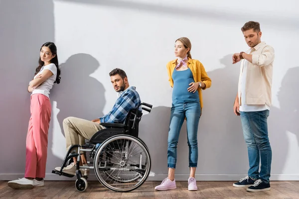 Multiethnic people and disabled man standing near wall in queue — Stock Photo
