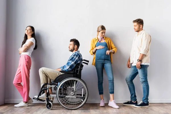 Pregnant woman checking time near disabled man and multiethnic people in hall — Stock Photo