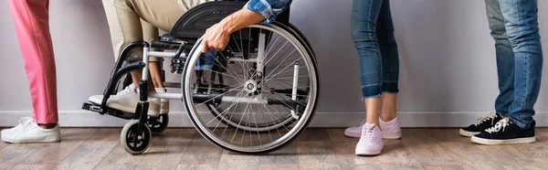 Обрізаний вид людей, що стоять біля людини в інвалідному візку в черзі, банер — стокове фото