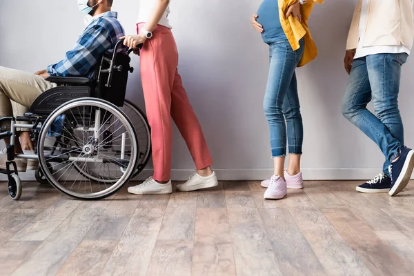 Cropped view of disabled man in medical mask sitting in wheelchair near people in hall — Stock Photo