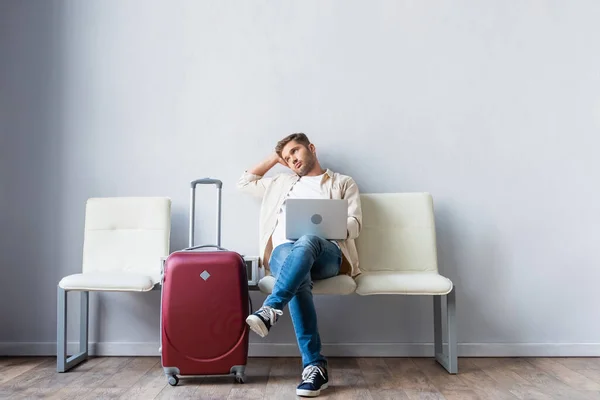 Чоловік з ноутбуком дивиться далеко біля валізи під час очікування в аеропорту — стокове фото