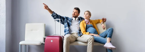 Homem apontando com o dedo perto da esposa grávida e mala no aeroporto, banner — Fotografia de Stock