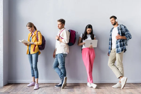 Étudiants multiculturels avec ordinateur portable et livre debout dans le hall — Photo de stock