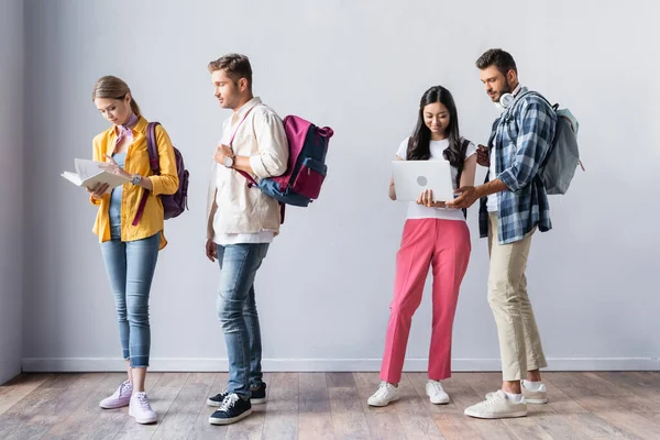 Multicultural students with laptop, backpacks and book waiting in hall — Stock Photo