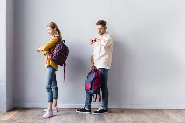 Students with backpacks looking at wristwatch in hall — Stock Photo
