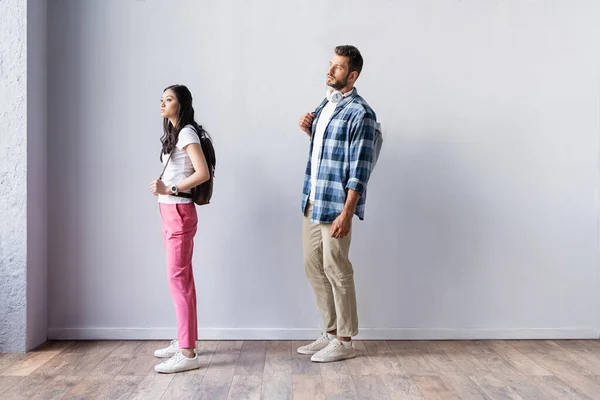 Asiático estudiante de pie cerca de hombre con mochila y auriculares en cola - foto de stock