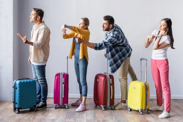 Pessoas multiculturais agressivas apontando para relógio de pulso perto de malas no aeroporto — Fotografia de Stock