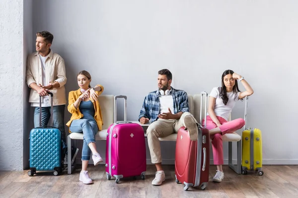 Personas multiculturales estresadas mirando hacia otro lado cerca de maletas en la sala del aeropuerto - foto de stock